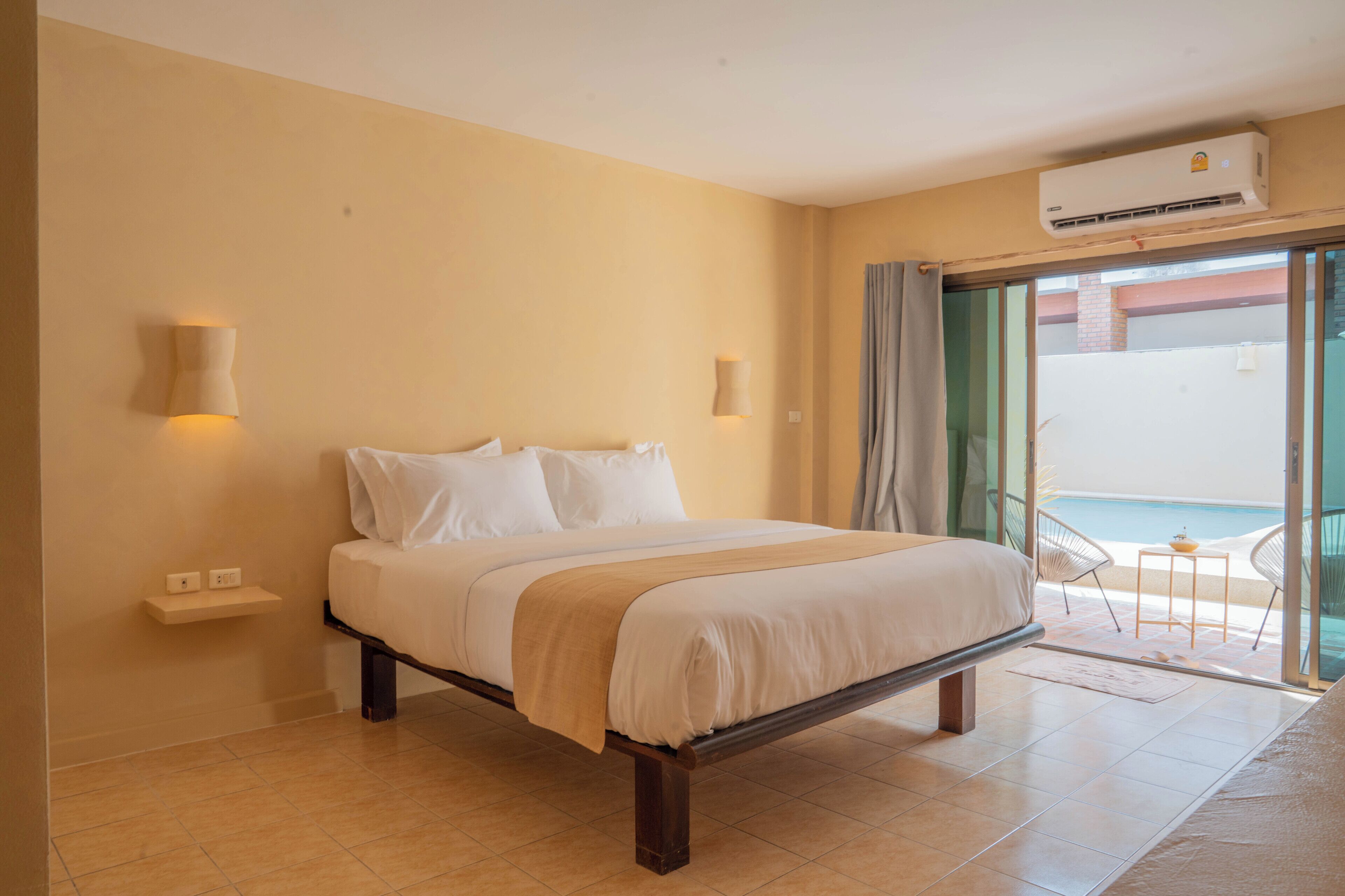 Una camera da letto con un letto, comodini, luci a parete, un condizionatore e vista sulla spiaggia attraverso una porta in vetro.
