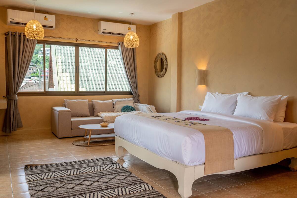 A bedroom with a bed, a sofa, a small table, and a window with curtains.