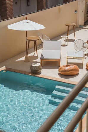 A poolside area with a pool, lounge chairs, a small table, and an umbrella. - Casa Solana Patong (Patong)