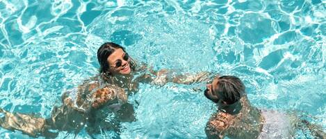 Una piscina al aire libre, sombrillas, sillones reclinables de piscina