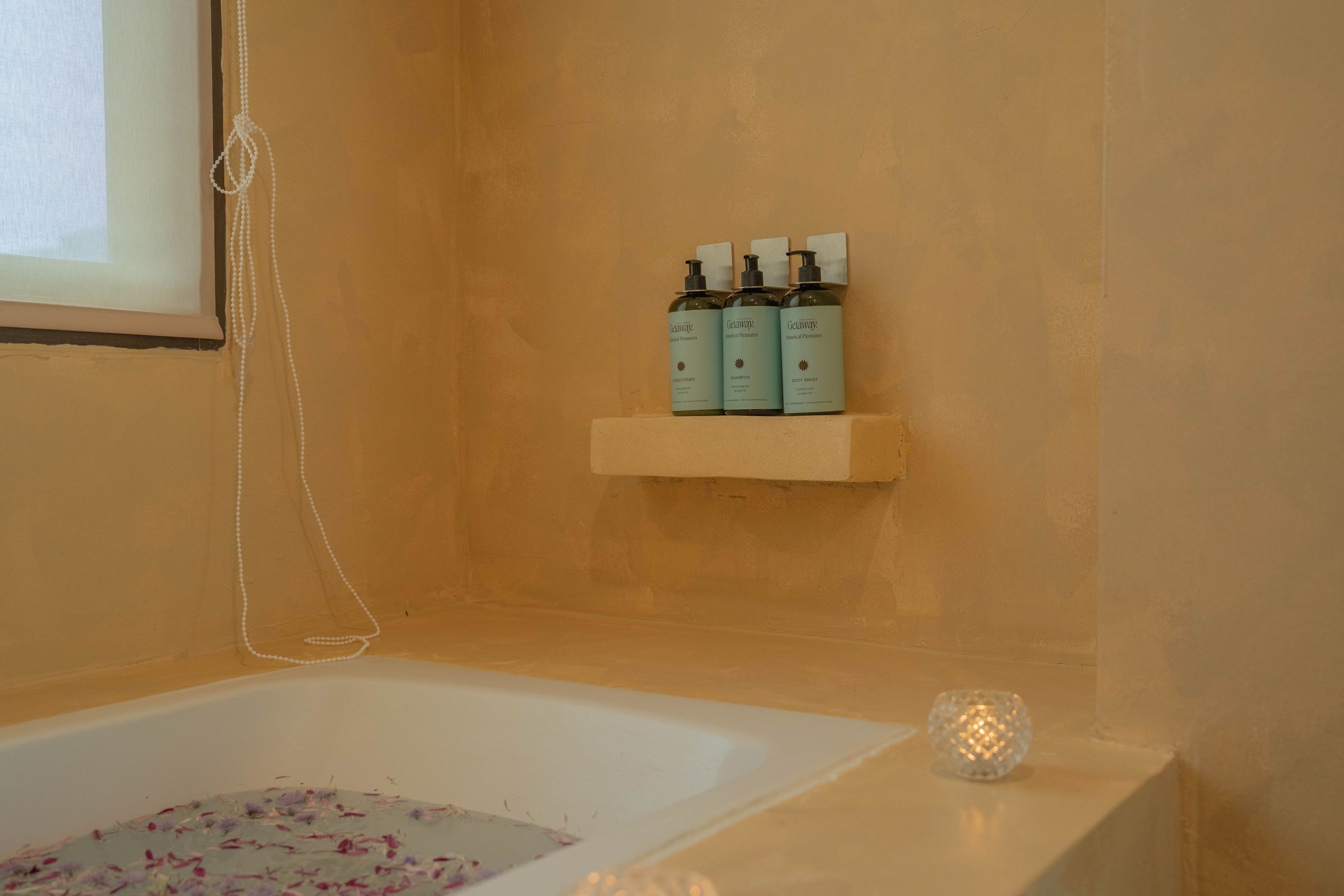 Un baño con una bañera, un estante con tres botellas y un objeto de vidrio decorativo.