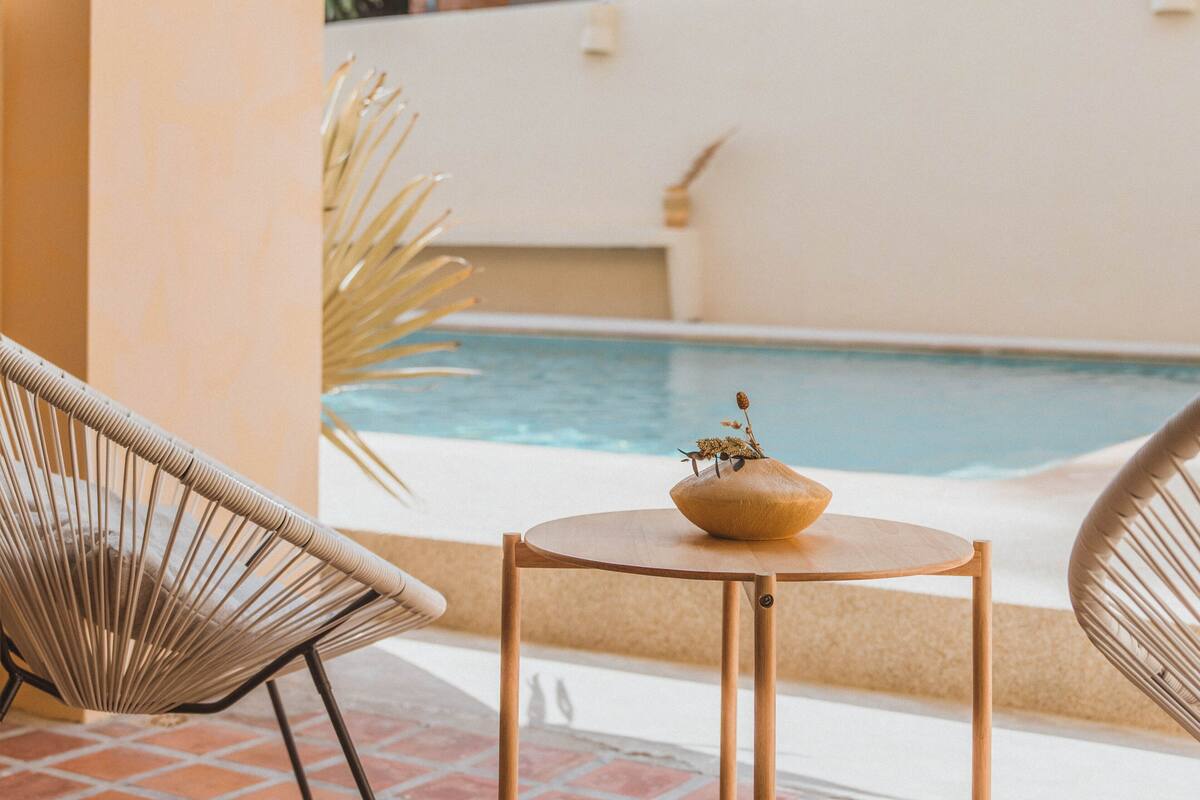 A poolside area with a round table and two wicker chairs, a small potted plant, and a view of a swimming pool.