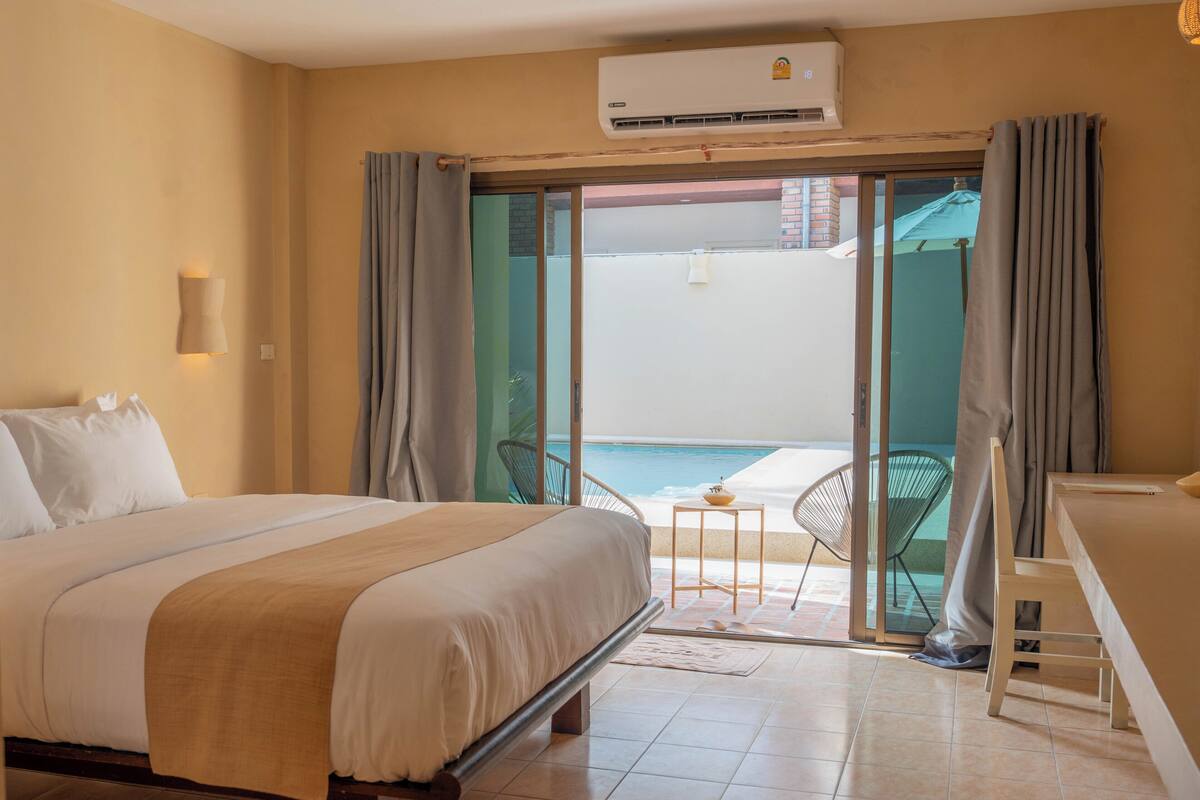 A hotel room with a bed, a small table with a bowl, and a view of a pool through a glass door.