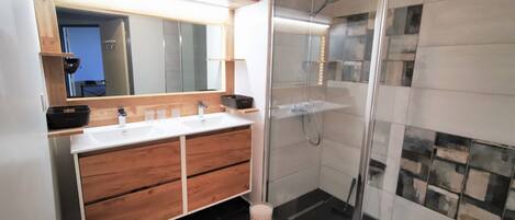Une salle de bain moderne avec deux vasques, un meuble-lavabo en bois, une cabine de douche en verre et un miroir au-dessus du meuble-lavabo.