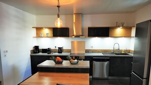 A modern kitchen with a central island, two chairs, a coffee machine, and a dishwasher. - Appt "corail" au Pied du Lagon de St Leu (Saint-Leu)