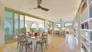 Una habitación amplia con comedor, estantería y grandes ventanales con vistas al exterior.
