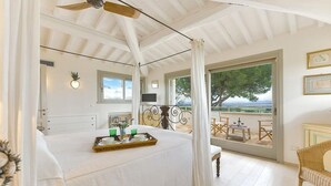 Un dormitorio con una cama grande, un balcón con mesa y sillas, y vista al mar.