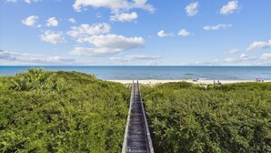 Een houten looppad dat naar een strand leidt, met een heldere lucht en losse wolken.