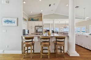 A spacious kitchen with a large island, white cabinetry, and a view to the living area. - Welcome to Land Yacht! (St. George Island)