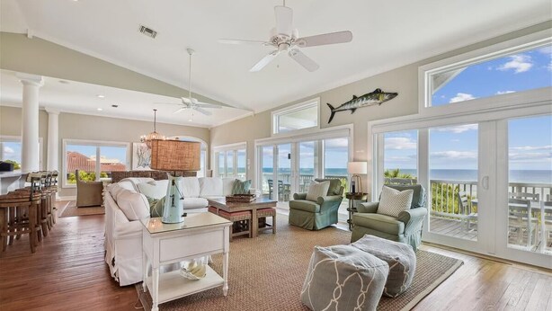 Een ruime woonkamer met een groot raam met uitzicht op de oceaan, een plafondventilator en een eethoek met een panoramisch uitzicht.