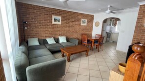 A living room with a sectional sofa, a wooden coffee table, and a dining area with chairs and a table.