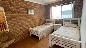 Een kamer met twee bedden, een stoel, een klein tafeltje en een raam met jaloezieën.