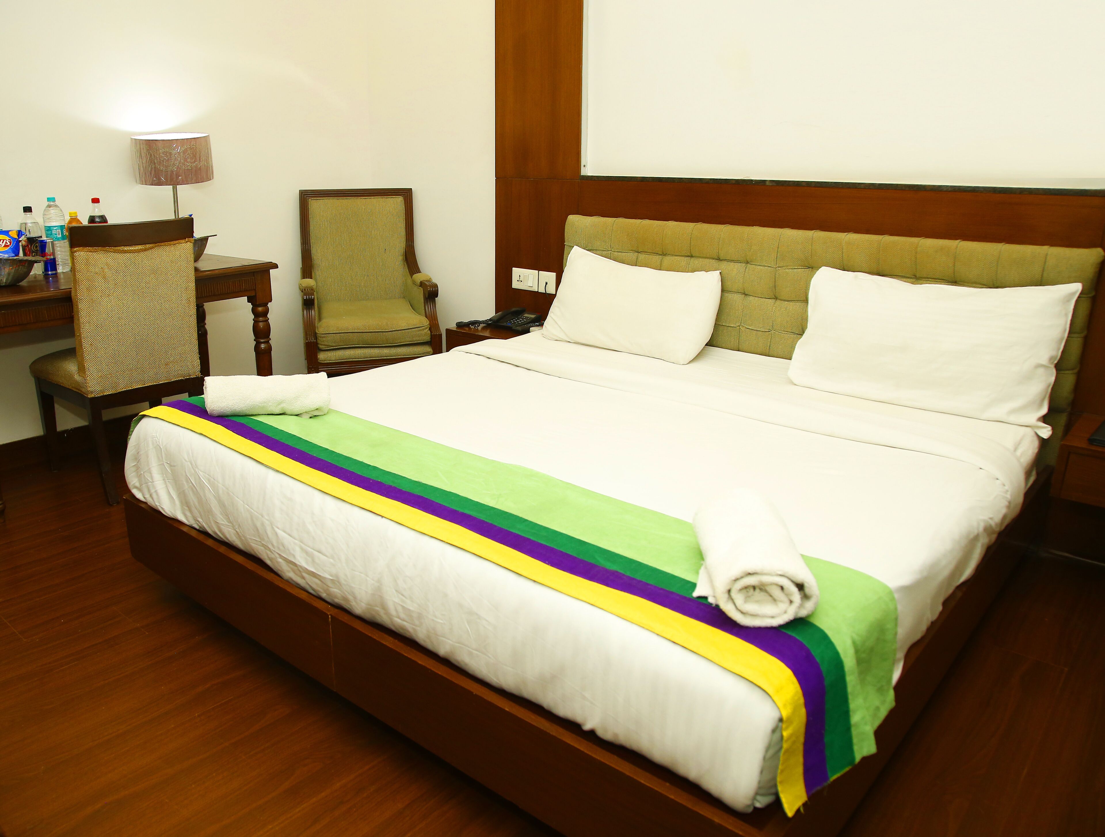 A neatly made bed with a colorful blanket, a wooden headboard, and a small desk with a lamp and toiletries.