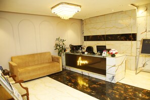 A reception area with a marble reception desk, a sofa, and a chandelier. - Amara Hotel (New Delhi)
