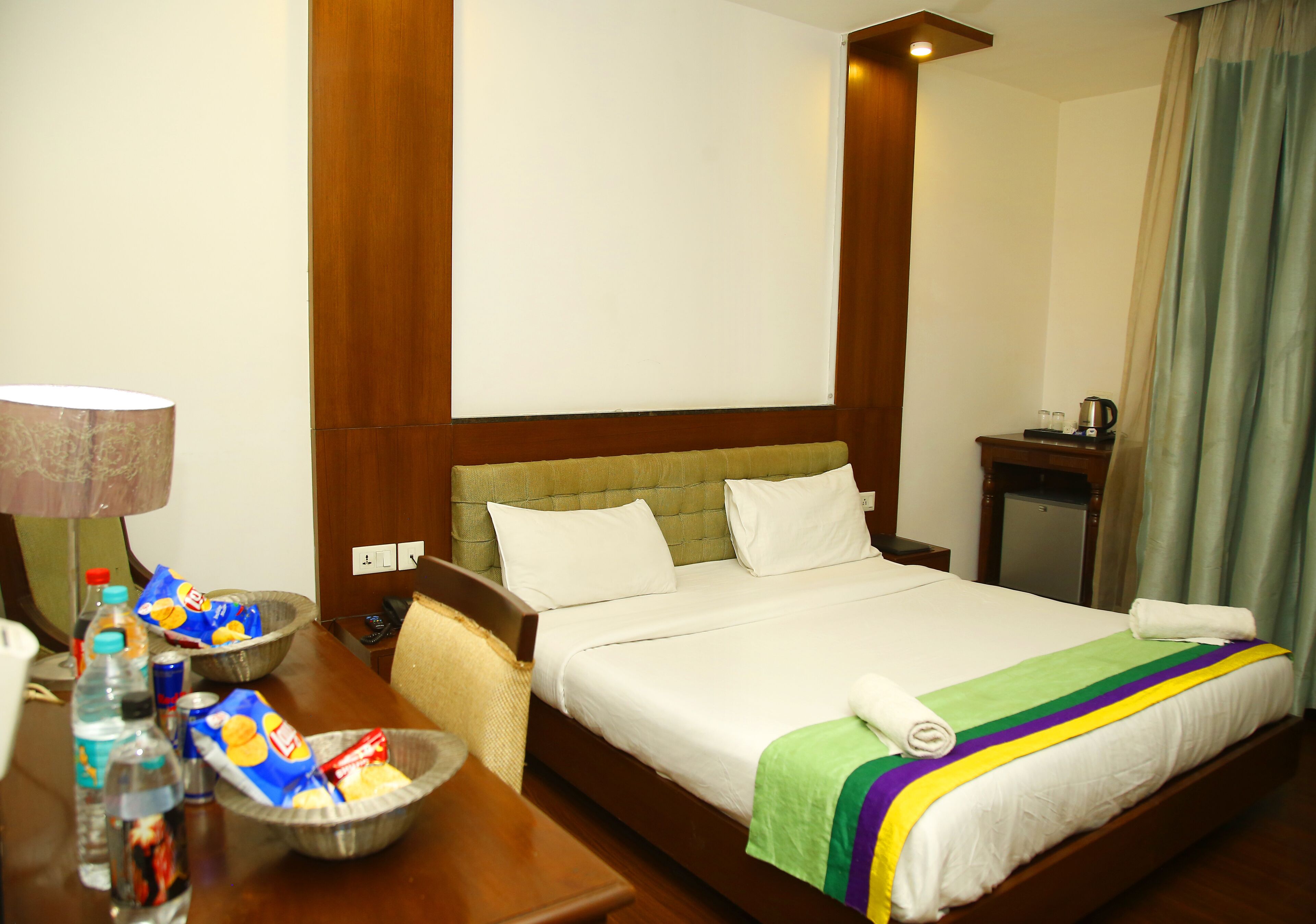 Una habitación de hotel con cama, mesitas de noche, una lámpara y vistas al exterior.