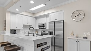 Una cocina moderna con armarios blancos, electrodomésticos de acero inoxidable y una isla central con taburetes.