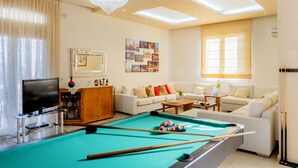 Un salón con mesa de billar, televisor, sofá y candelabro.