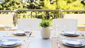 Una mesa de comedor dispuesta con platos, vasos y cubiertos, con una planta en maceta en el centro.