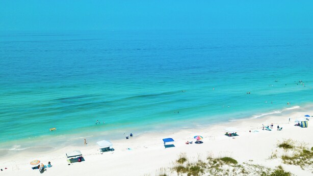 Een strand met helder turquoise water, wit zand en verschillende strandparasols en tenten.
