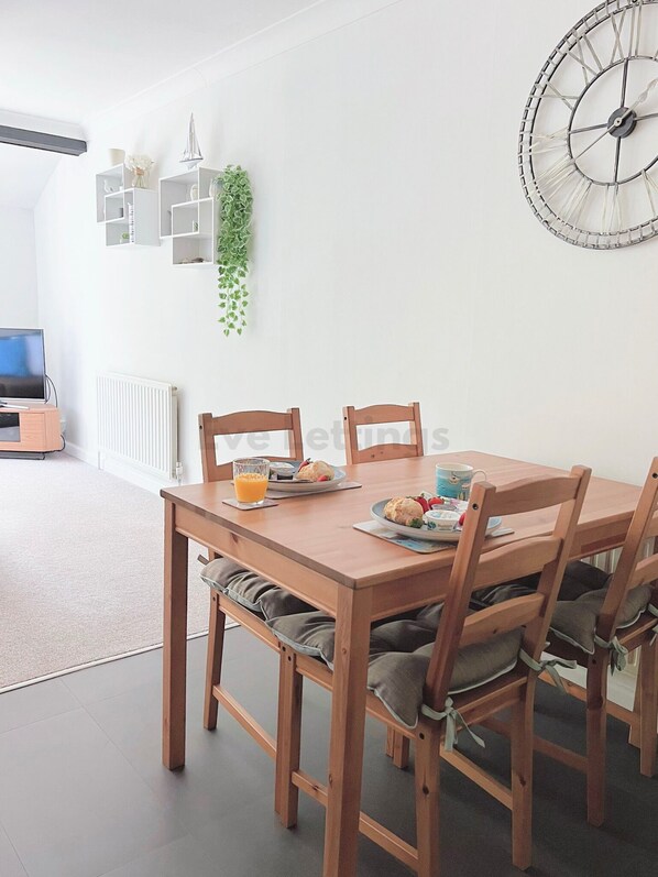 Un coin repas avec une table et des chaises en bois, une horloge au mur et un radiateur.