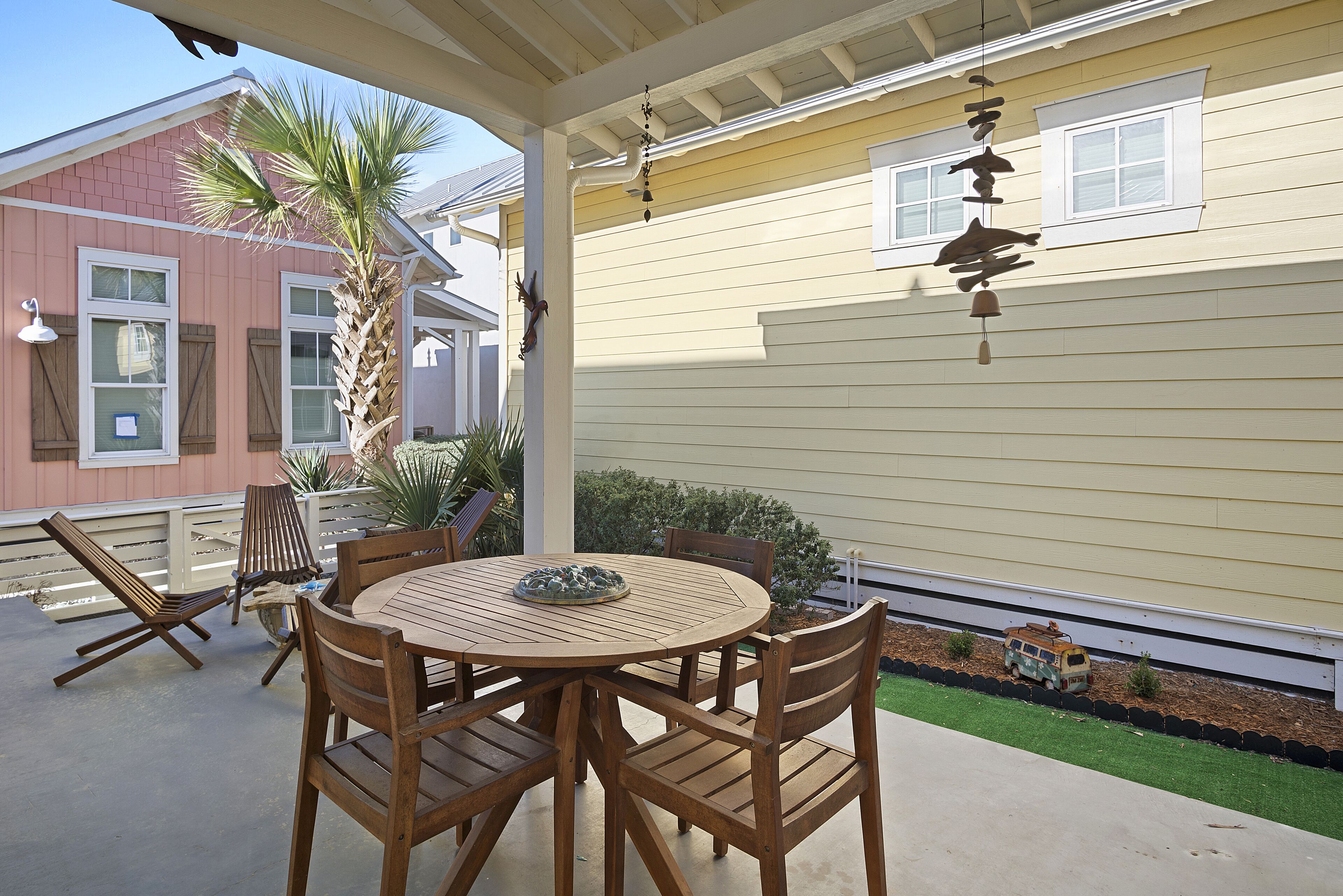 A covered patio with a wooden table and chairs, a small decorative van, and a palm tree.
