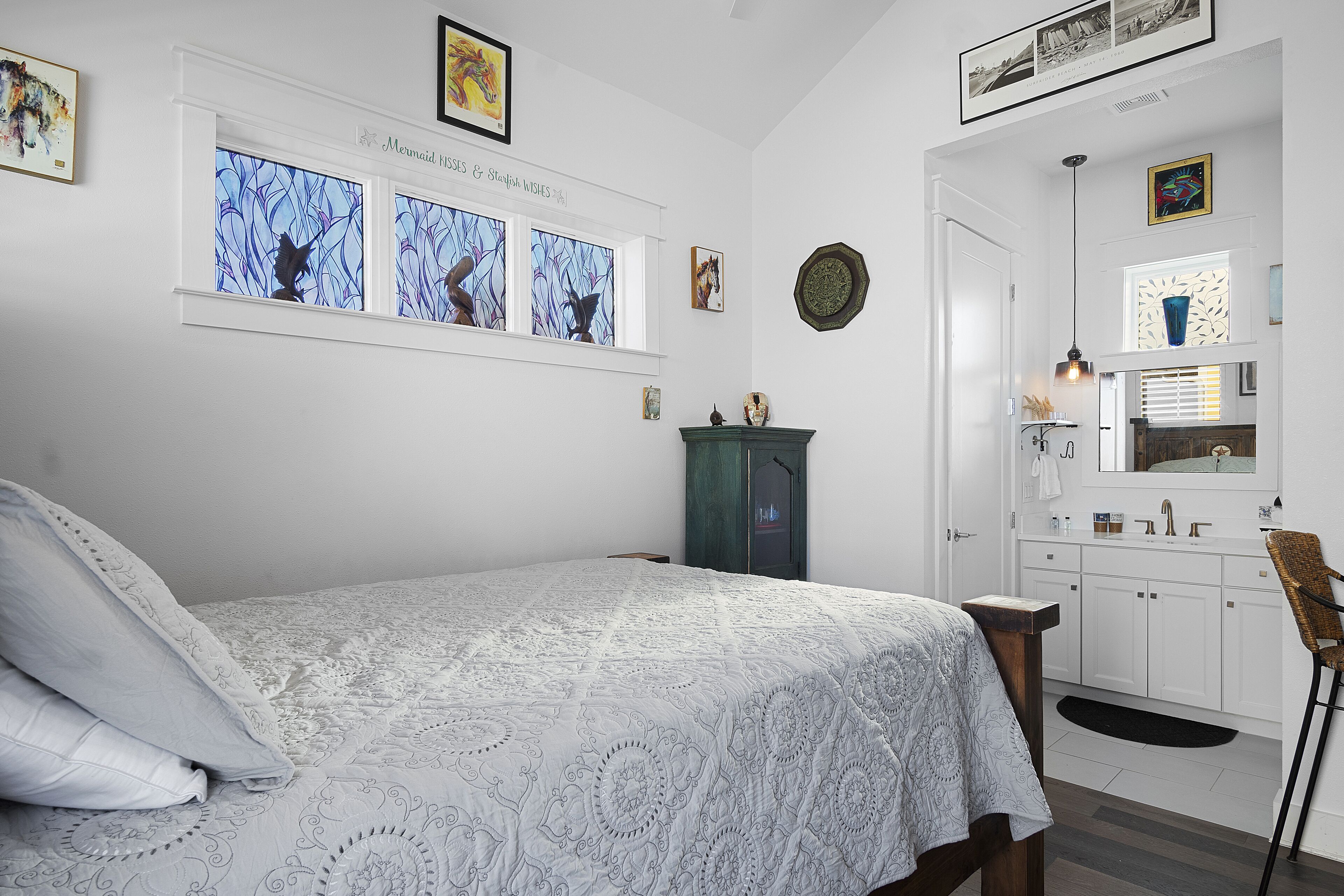 Un dormitorio con cama, cómoda, tocador y ventana decorada con una obra de arte.