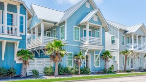 Een rij blauw-witte strandhuizen met balkons, palmbomen en een heldere lucht.