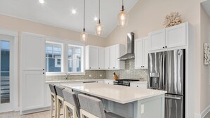 Een moderne keuken met witte kasten, een groot kookeiland met barkrukken, roestvrijstalen apparatuur en hanglampen.