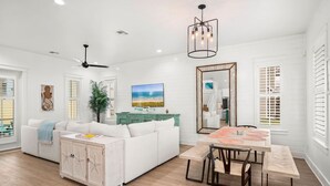 A spacious living room with a white sofa, a dining table with chairs, a ceiling fan, and a large mirror. - Resort Pools, Golf Cart Boardwalk to the Beach (Port Aransas)