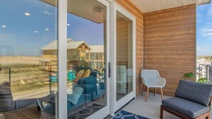 Un salon moderne avec une porte vitrée donnant sur un balcon, un mur en bois et un canapé gris.