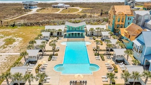 Oversigtsbillede af et resort med en central swimmingpool, flere opholdsområder og ejendomme ved stranden.