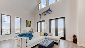 A modern living room with a white sectional sofa, a black ottoman, and a large window with a city view.
