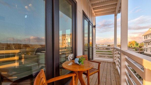A wooden deck with a round table and chairs, large windows, and a view of a cityscape.