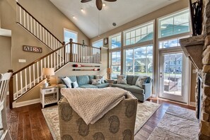 A spacious living room with a staircase, large windows, and a fireplace.