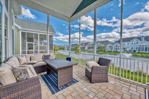 A covered outdoor patio with wicker furniture, a table, and a view of a residential area.
