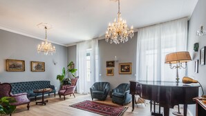 A spacious living room with a grand piano, a blue sofa, and two armchairs.