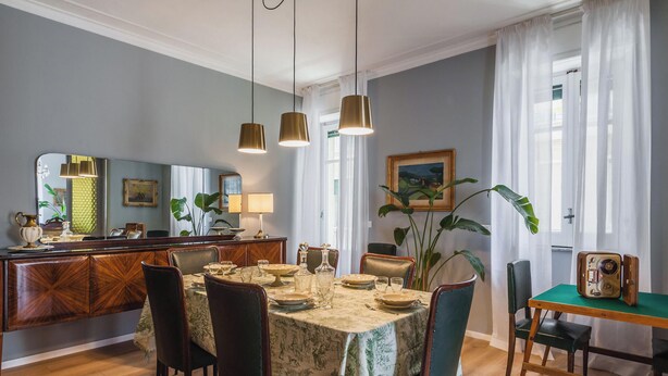 A dining area with a table set for four, a wooden cabinet, and a green table with a vintage suitcase.