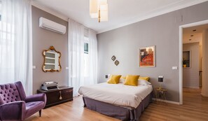 Quarto moderno com uma cama grande, uma escrivaninha e uma cadeira. Há um espelho, um abajur e um cartaz na parede.