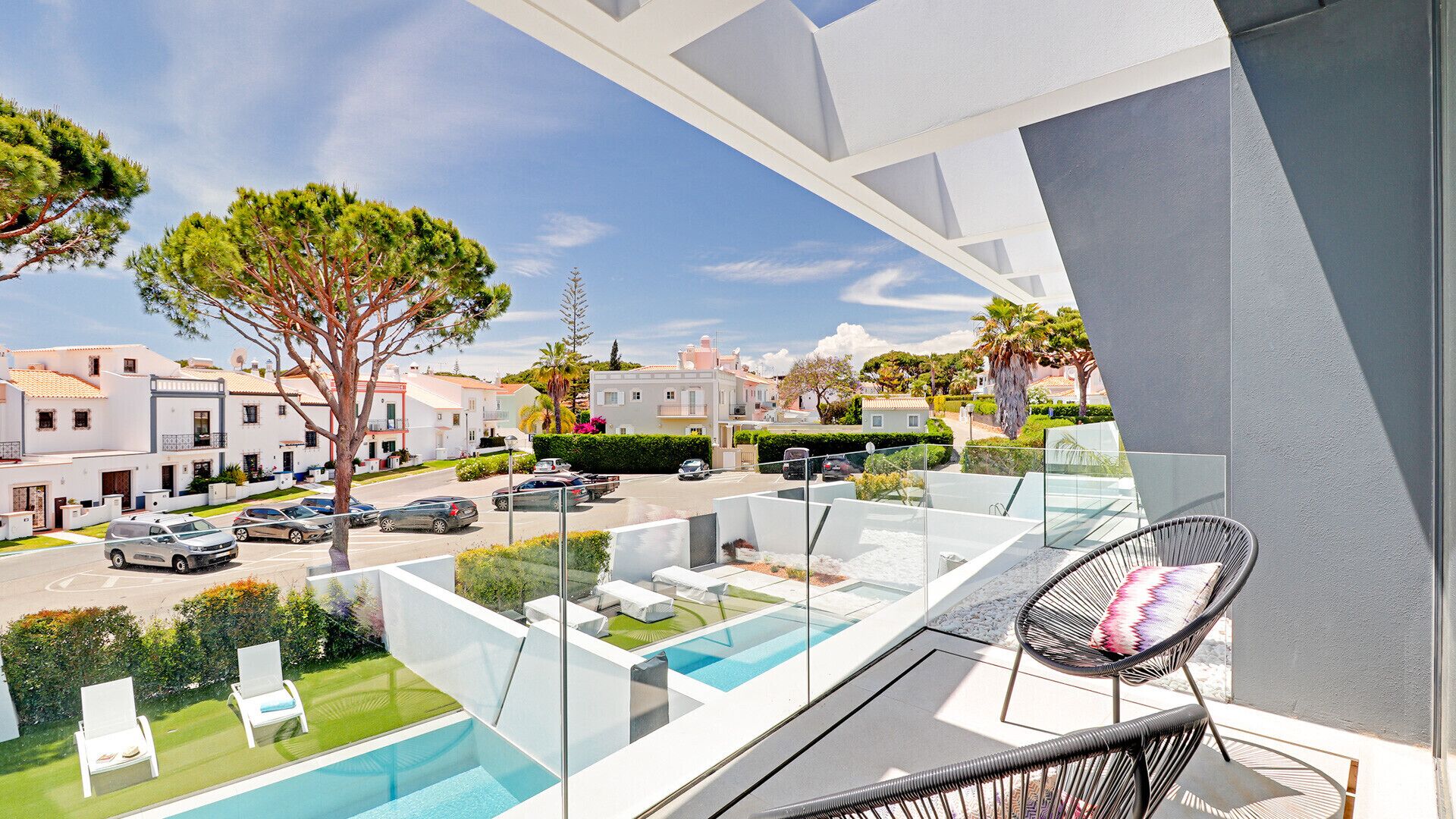 A modern balcony with a pool, lounge chairs, and a view of a residential street.