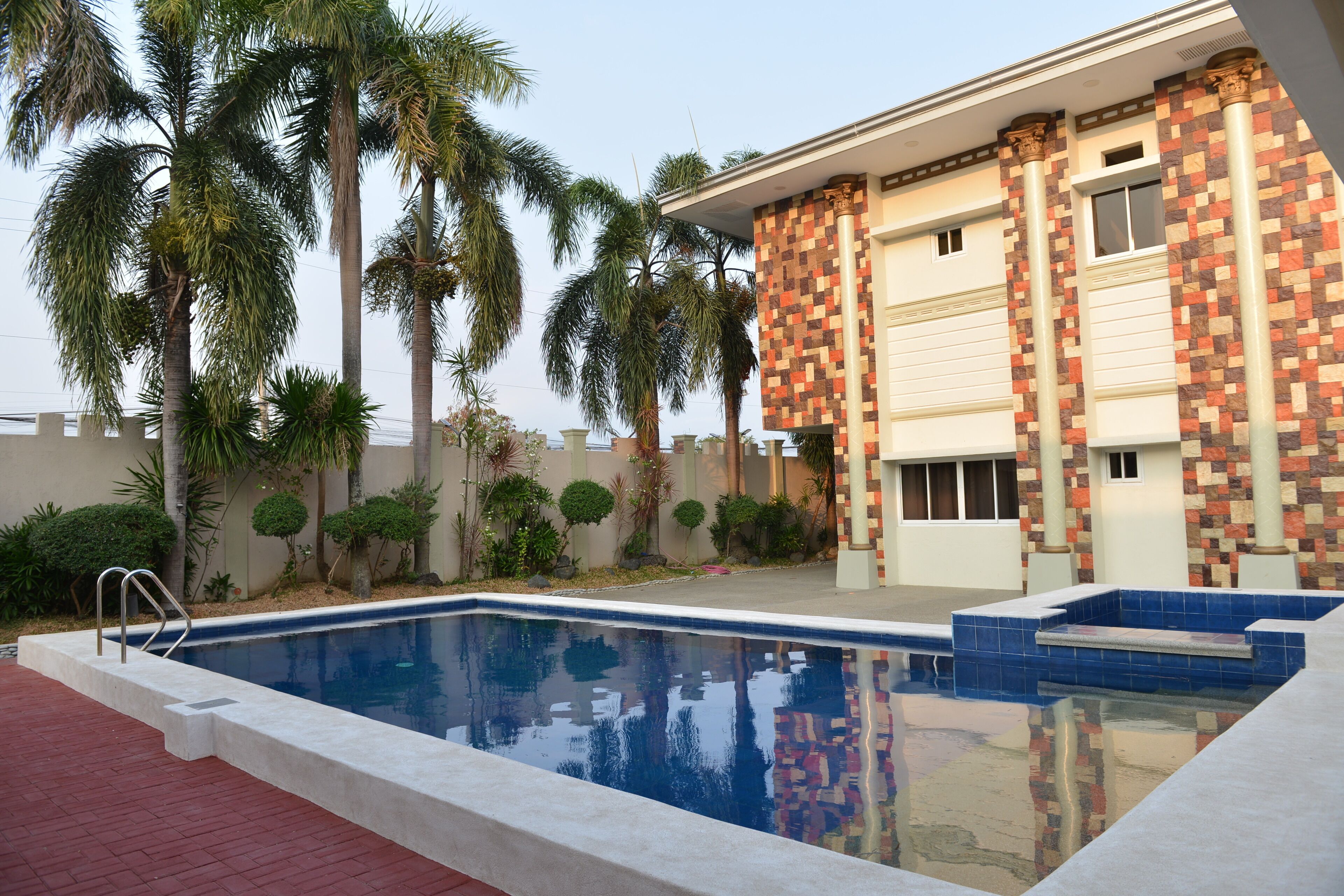 A swimming pool with a tiled deck, palm trees, and a building with a patterned facade.