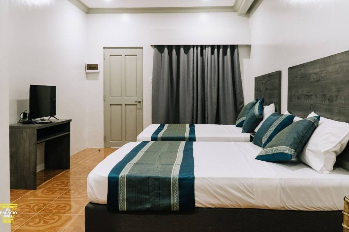 Una habitación de hotel con dos camas, un escritorio y un televisor, y una puerta.