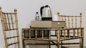 Una silla de bambú y una mesita con un hervidor, una botella de agua y una taza.