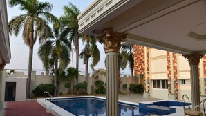 Un área de piscina con un paseo de baldosas rojas, palmeras y columnas de estilo clásico.