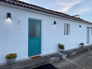 A white building with a teal door, numbered 3, and a 'hello' mat at the entrance.