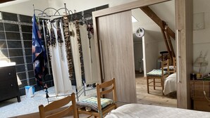 A bedroom with a bed, two wooden chairs, a mirror, and a clothing rack with various items. - Maison Sainte Foy La Grande (Pineuilh)