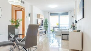 Una sala moderna con una mesa de centro de vidrio, un sofá y una zona de comedor con una mesa y sillas blancas.