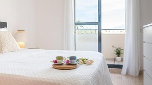 Habitación de hotel con una cama grande, un balcón con una planta en maceta y una ventana con cortinas.