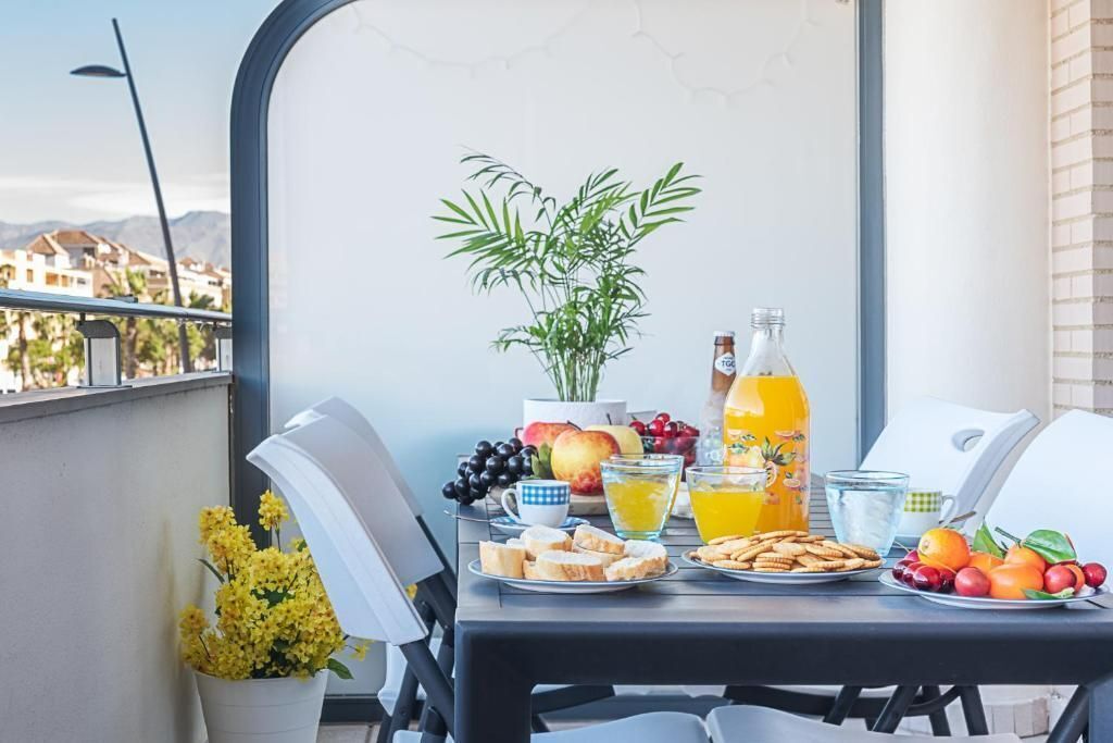 Un balcón con una mesa lista para el desayuno, con frutas, jugo y una botella.