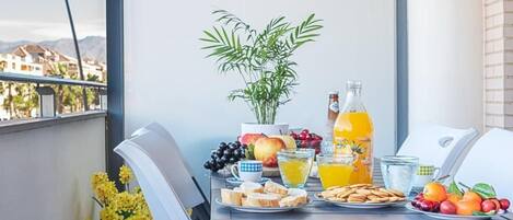 Un balcón con una mesa lista para el desayuno, con frutas, jugo y una botella.