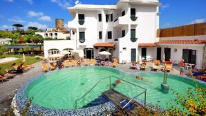 A pool area with lounge chairs and umbrellas, a white building with balconies, and a tower in the background. - hotel park victoria (Forio)